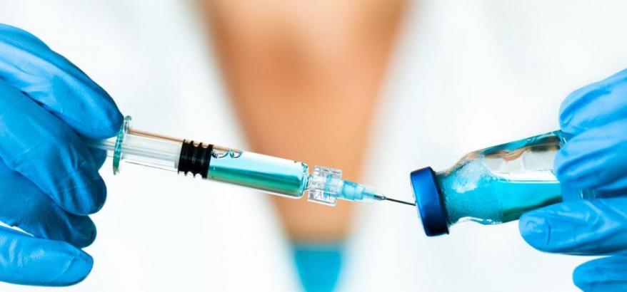 imagem de uma seringa sendo preenchida com vacina, por uma pessoa usando luvas azuis 