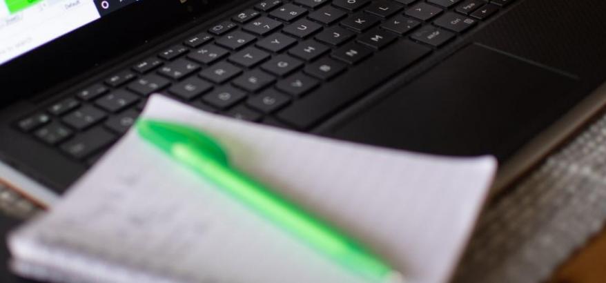 Imagem de um computador e de uma caneta verde, sobre um caderno branco, com o título, em letras brancasAlunos do colégio Pedro II participam de audiências on-line no Juizado Especial Federal de Nova Friburgo""
